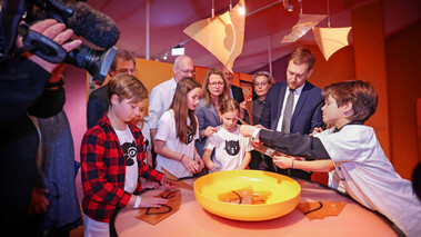 Kinder und Erwachsene in einer Fernsehsendung mit KatzeQ-Figur und farbigem Studiolicht.